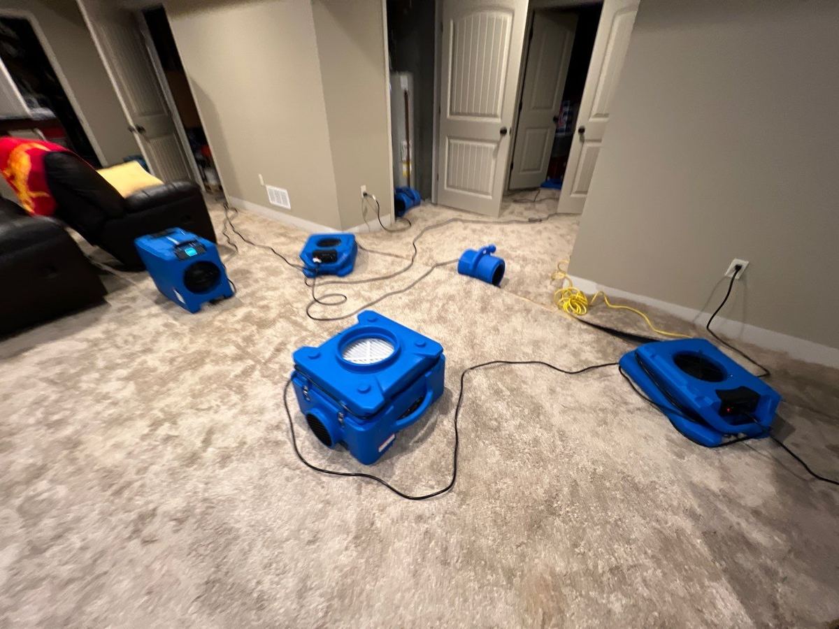 Dehumidifier and air movers drying a carpeted finished basement in Lee's Summit, MO after a sump pump failure