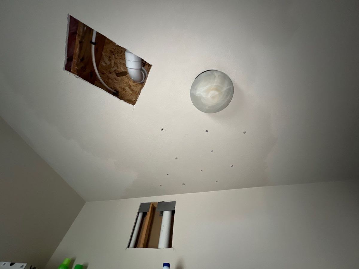 Laundry room ceiling and wall with drywall sections cut out and small drying holes after an upstairs supply line leak
