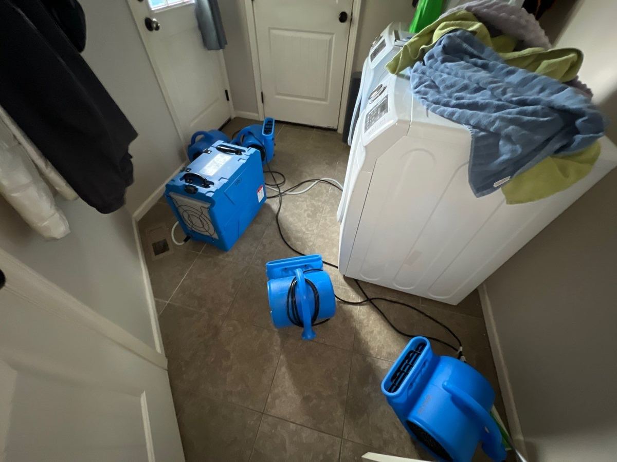 Air movers and a dehumidifier drying a laundry room tile floor beside a washer and dryer