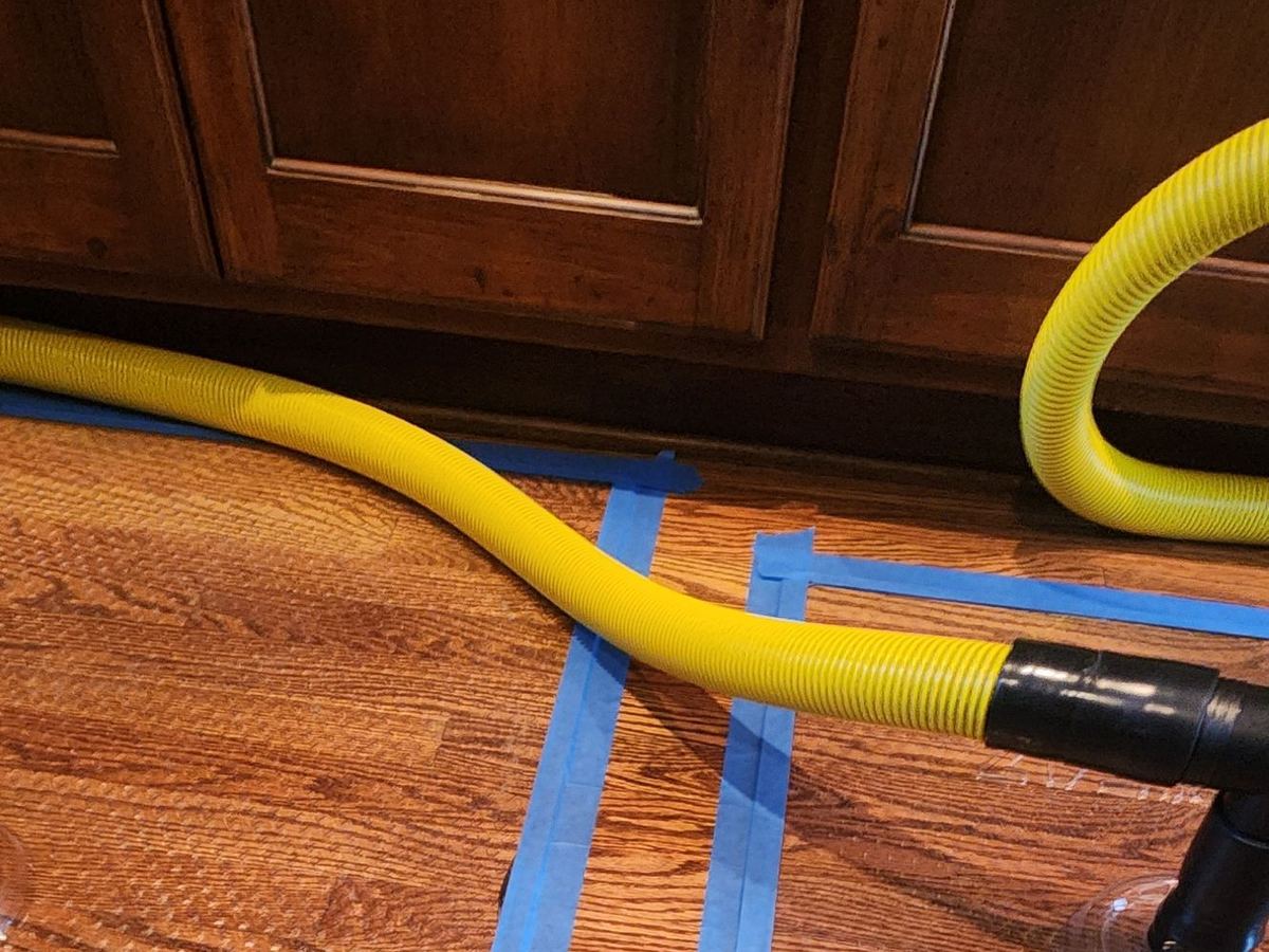 Drying mats taped to wet hardwood flooring along kitchen cabinets with a yellow suction hose