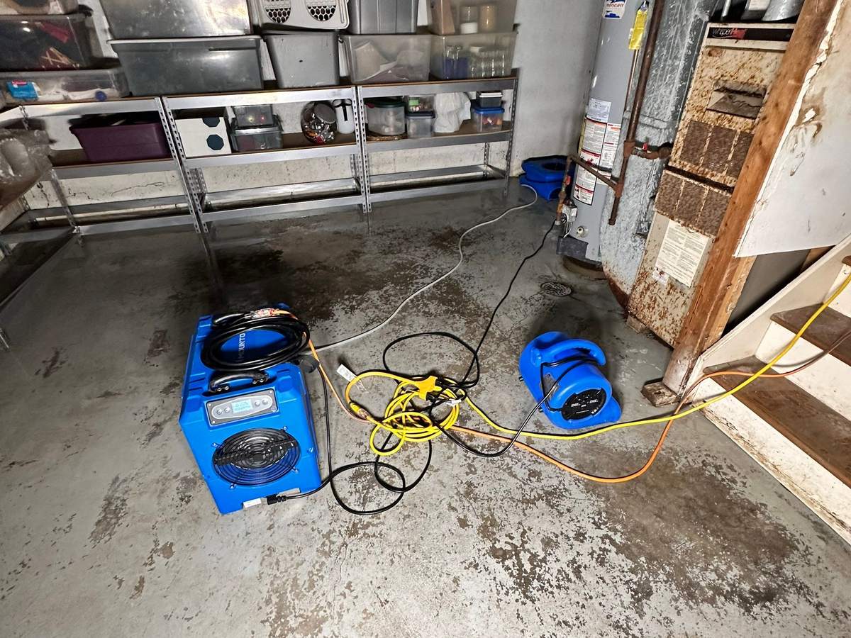 Dehumidifier and air mover drying a basement utility room floor next to a water heater and furnace